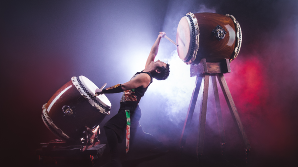 man drumming on two large drums while backlit with fog surrounding him