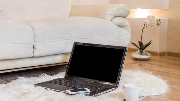 Laptop and iPhone on a rug next to a couch in someone's home.