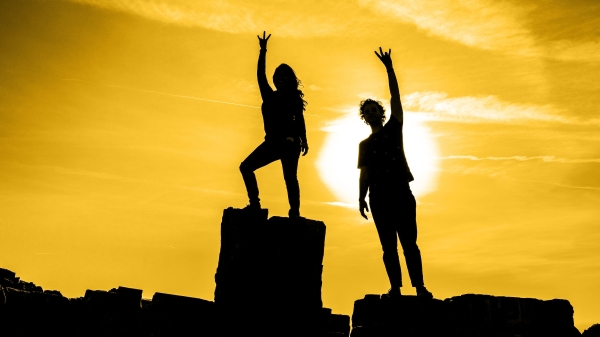 Silhouettes of two people making a pitchfork sign over their heads