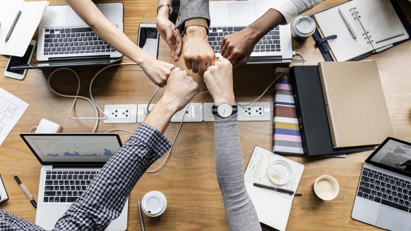 People fist-bump over a table filled with laptops