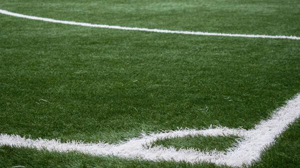 Close-up of the edge of a grassy playing field with white lines painted on it.