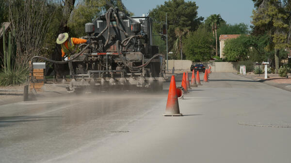 A truck drives down a neighborhood street spraying a light colored treatment to the pavement