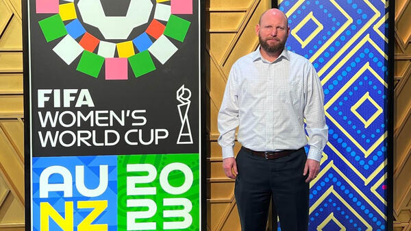 ASU alum Mike Davidson standing next to a sign for the FIFA Women's World Cup.