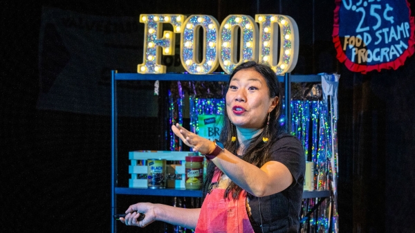Woman performing onstage in front of a sign that says "food."