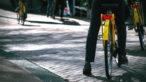 professionally dressed individual's leg touches brick pavement while pausing astride yellow community bicycle