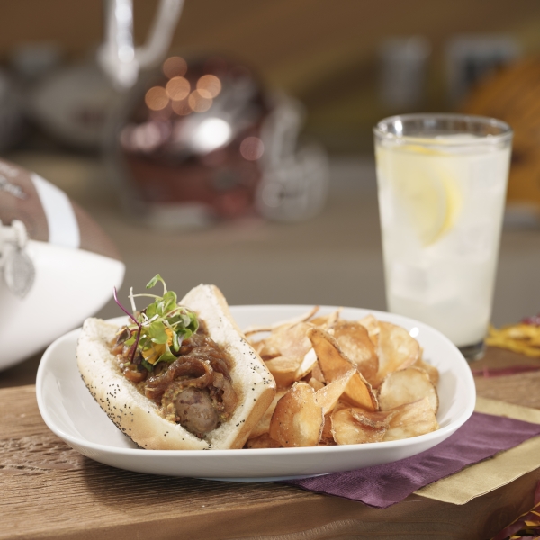 A plate with bratwurst and chips sits on a table next to an ASU football and a glass of water