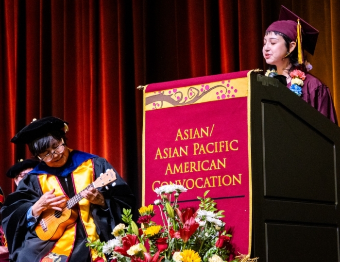 Woman playing a ukulele while another woman stands behind a lectern and speaks into a microphone at ASU's Asian/Asian Pacific American Convocation.