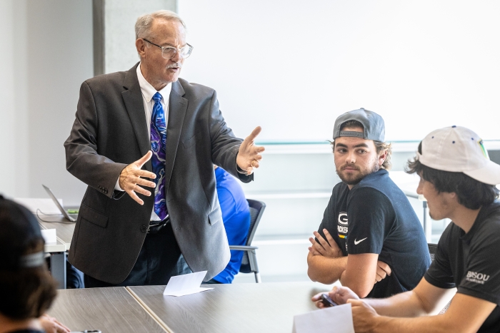 Man in suit and tie talking with students in classroom