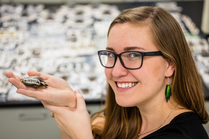 Woman wearing glasses holds up beetle in hand