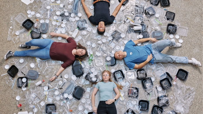 Four people lying on ground with plastic waste around them