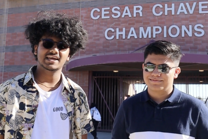Two high school students stand in front of a building with the words "Cesar Chavez Champions."