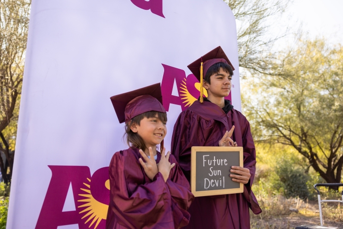 Two young children wearing maroon caps and gowns.