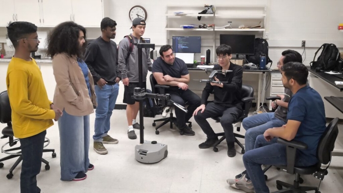 Professor Zhe Xu sitting in a lab surrounded by students.