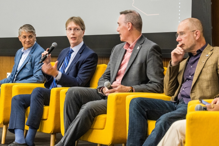 Four people sitting in yellow chairs on stage as part of panel