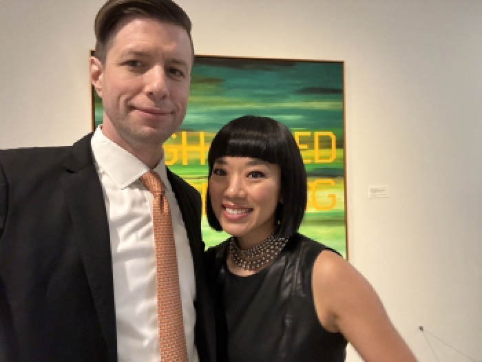 Man and woman pose for photo in front of painting