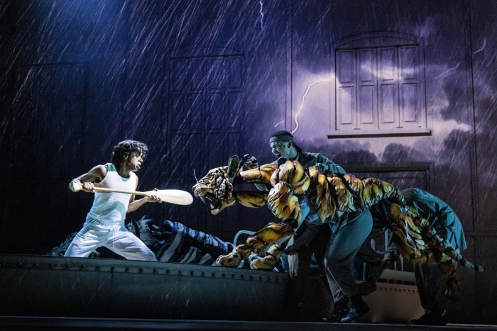 Boy fending off tiger on a boat in the rain during stage production