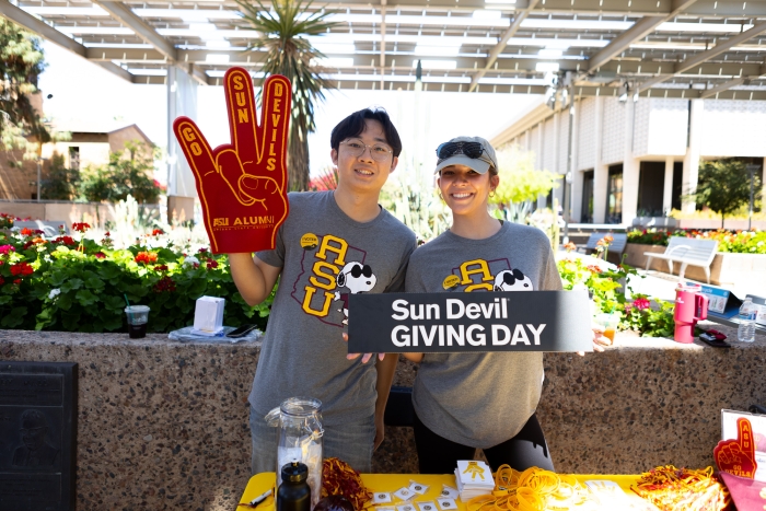Two people pose with foam finger and Sun Devil Giving Day sign