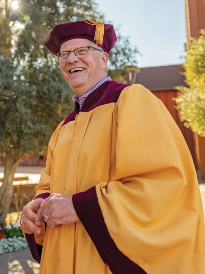 Older man wearing glasses and gold graduation gown