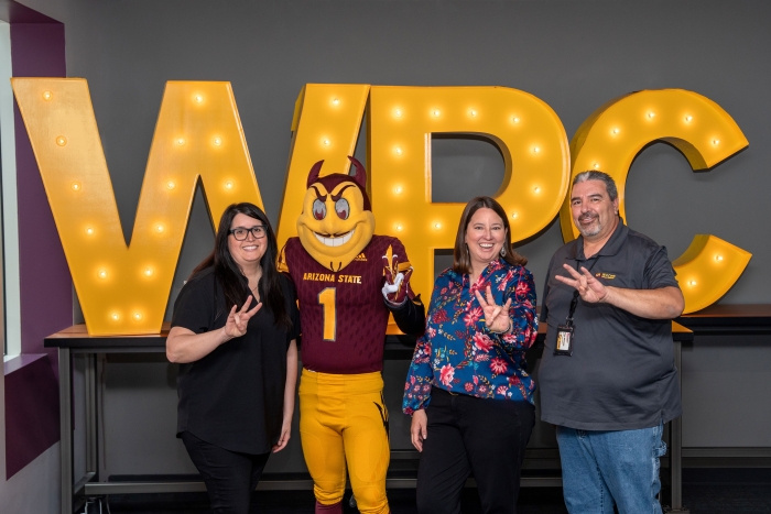 Three people pose with ASU's Sparky in front of a large "WPC" sign.