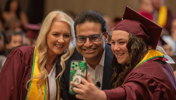 Two women in ASU graduation caps and gowns take a selfie with the CEO of Starbucks