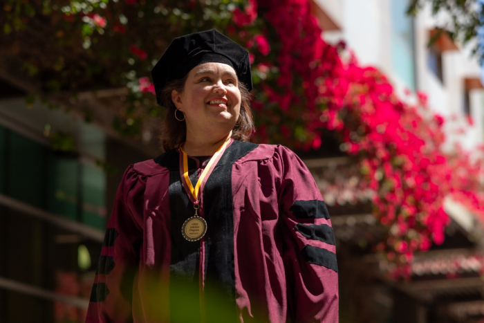 An ASU graduate in commencement regalia and wearing a medal smiles off camera