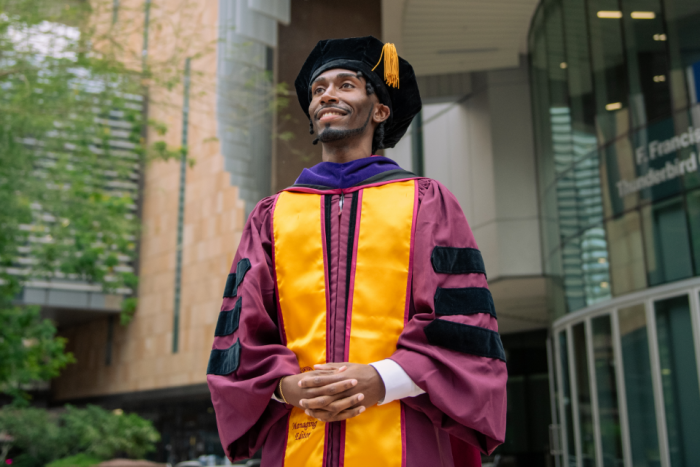 An ASU law graduate wearing commencement regalia smiles off camera
