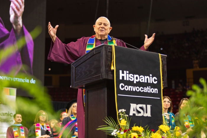 Older man speaking at lectern with arms raised during Hispanic Convocation