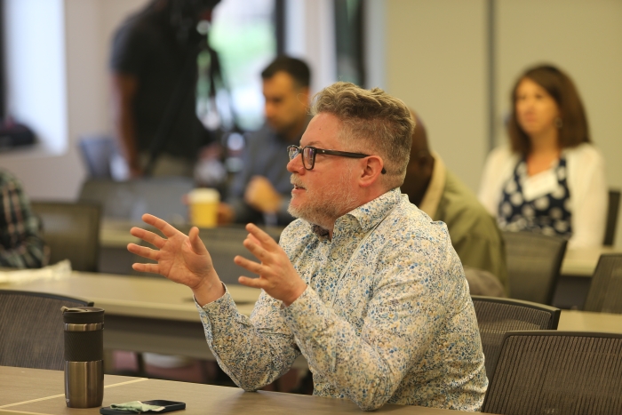 Matthew Shindell sits in an audience, hand gesturing as he asks a question