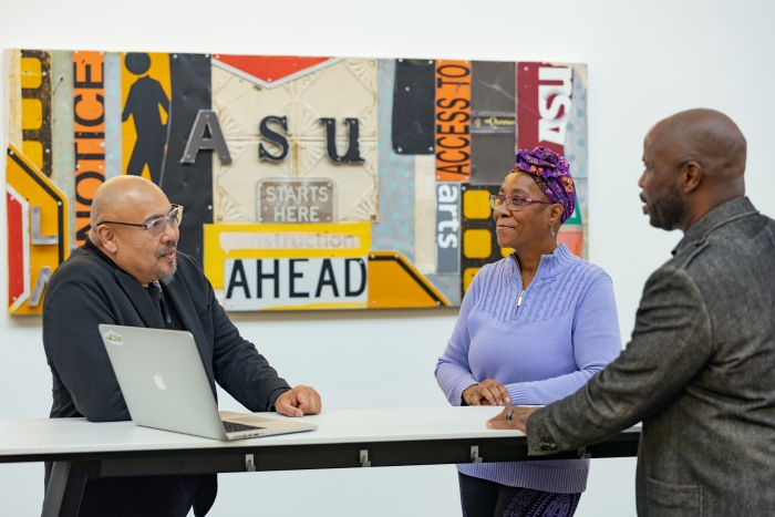 Three people speak while standing at a hightop table with a laptop open