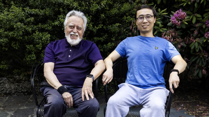 Dimitri Bertsekas and Yuchao Li sitting next to one another with a flowering bush behind them