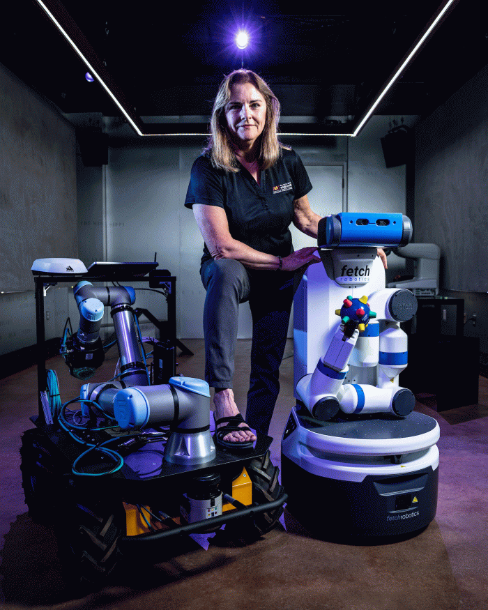 ASU Professor Nancy Cooke poses for a photo with several robots