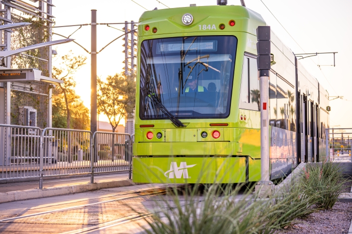 Bright green streetcar in a Tempe neighborhood at dawn.