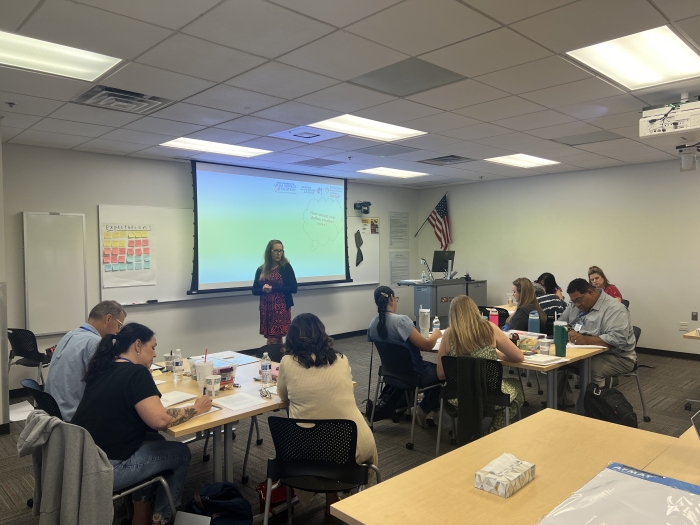 Teachers sit at classroom desks and listen to an instructor