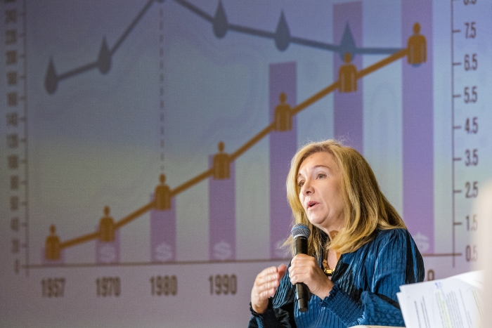 Woman speaking into microphone with bar graph on a presentation screen behind her