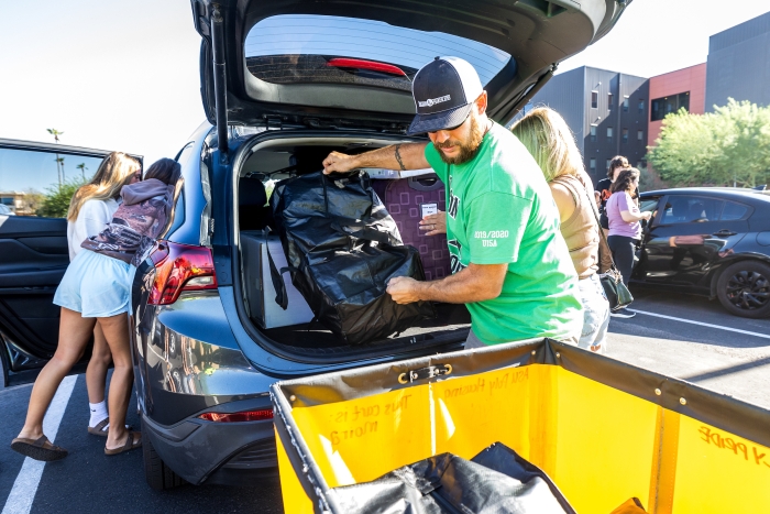 A father unloads items from the back of a car and places them in a yellow trolley