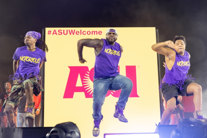 Three Black dancers perform on stage wearing purple shirts