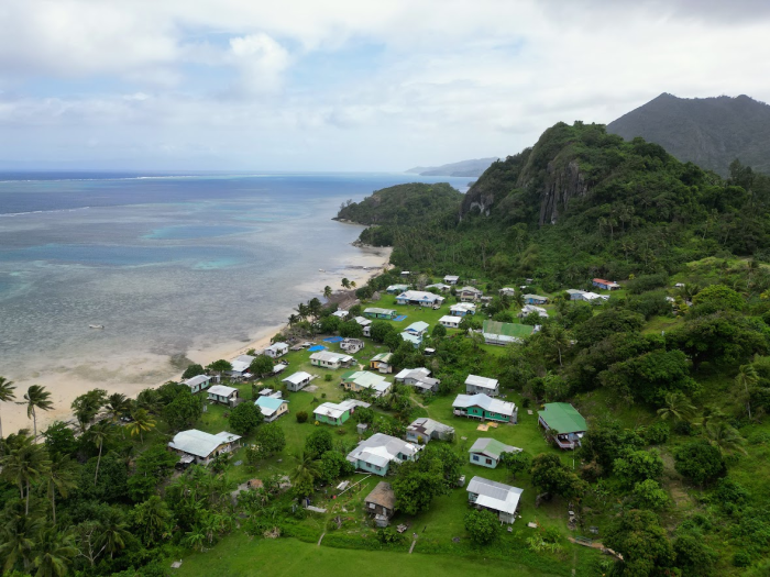 an aerial view of a Fijian community: groups of buildings surrounded by lush jungle and bordering a beach