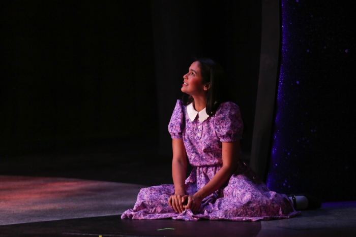 A Latina young woman sits along on the stage