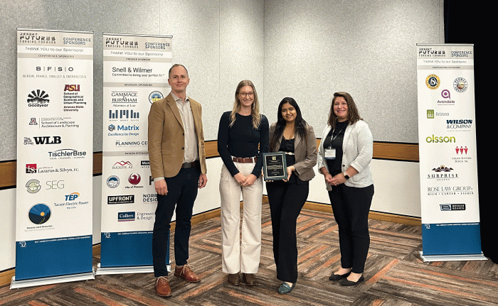 Four people stand in a line for a photo with one person holding an award