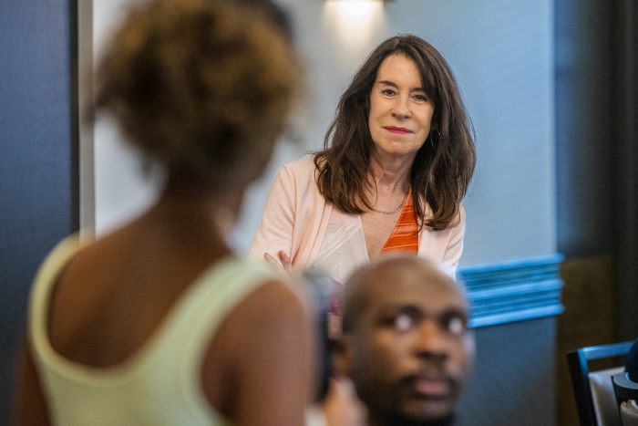 A white woman with long dark hair looks at a person asking a question, whose back is turned to the camera 