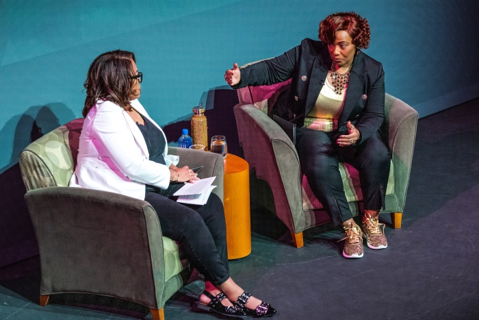 Two Black women sitting in chairs on stage talking during event