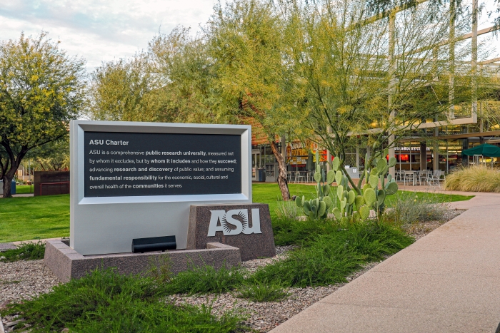 Statue with ASU charter next to walkway leading to Student Union. Native Arizona greenery surrounds the walkway.