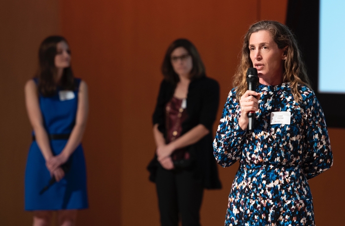 Leah Gerber holds a microphone and speaks onstage.