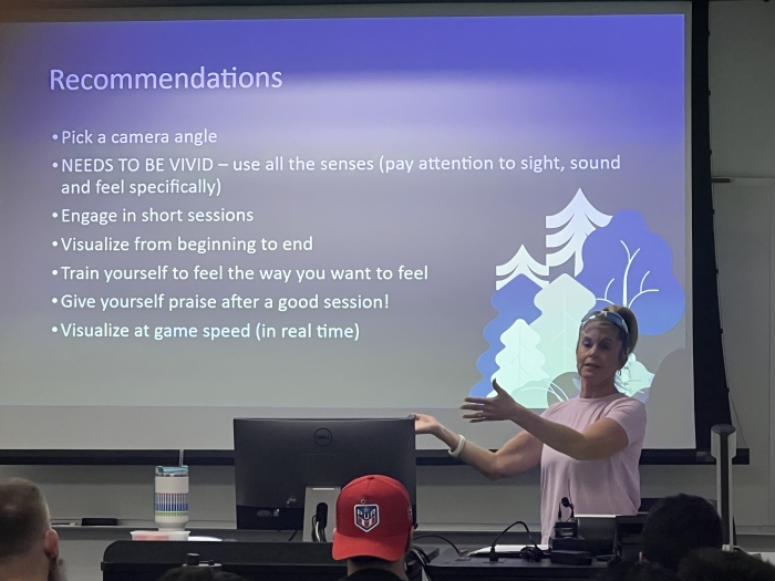 Woman giving a lecture while pointing to a large screen.