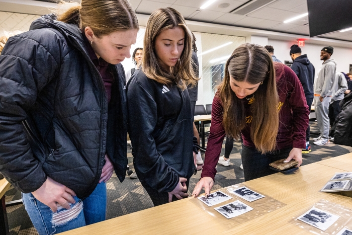 Three women look at black and white photographs on a table