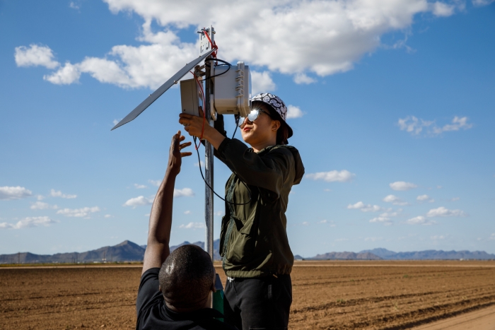 student researchers help set up equipment on a pole above a dirt farm field