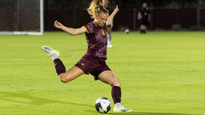 ASU grad Lieske Carleer kicking a soccer ball on a field.