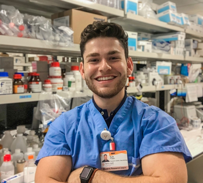 A young man in scrubs poses for a photo in a lab