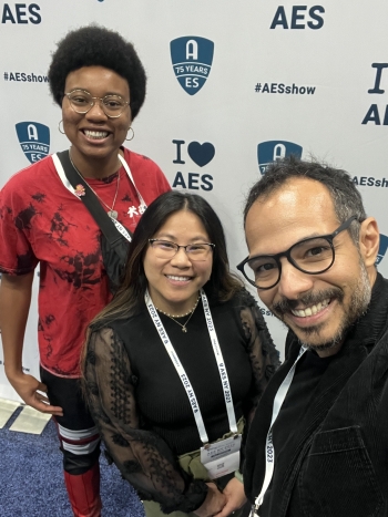 Three people smile at the camera in front of a backdrop with the letters "AES."