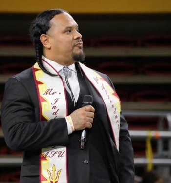 A man wearing a graduation stole looks to the side while holding a mic